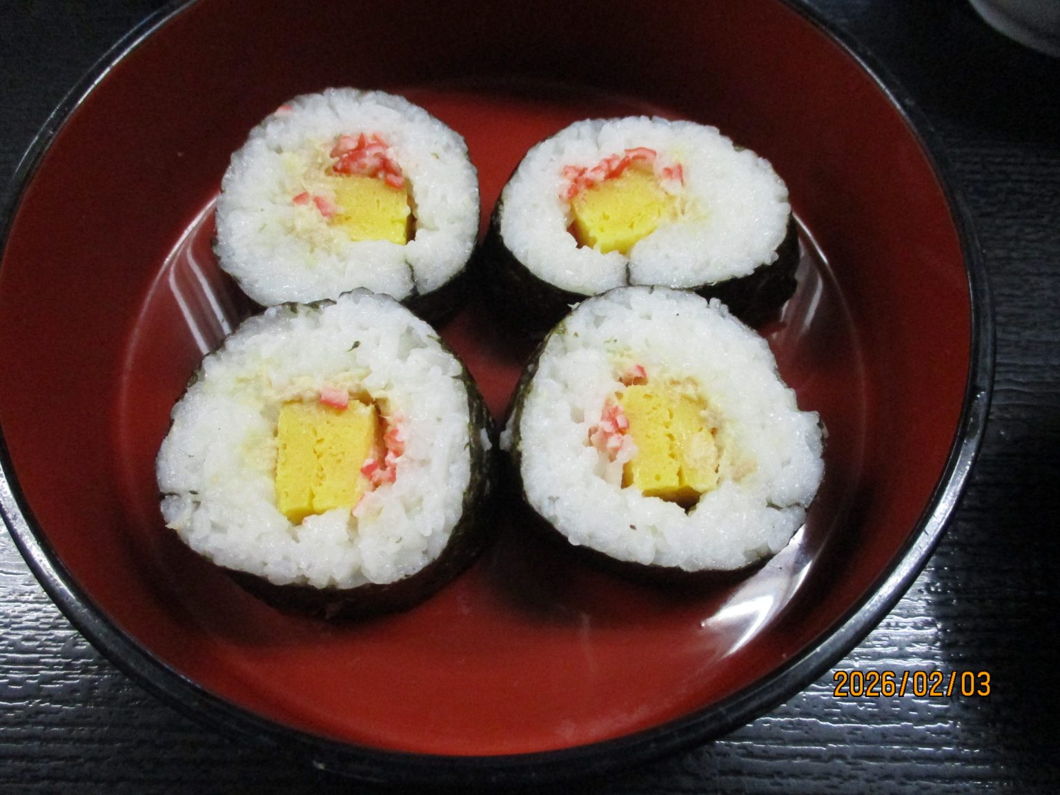 赤い皿に盛られた寿司巻き。卵と桜でんぶが入った介護食の一例。